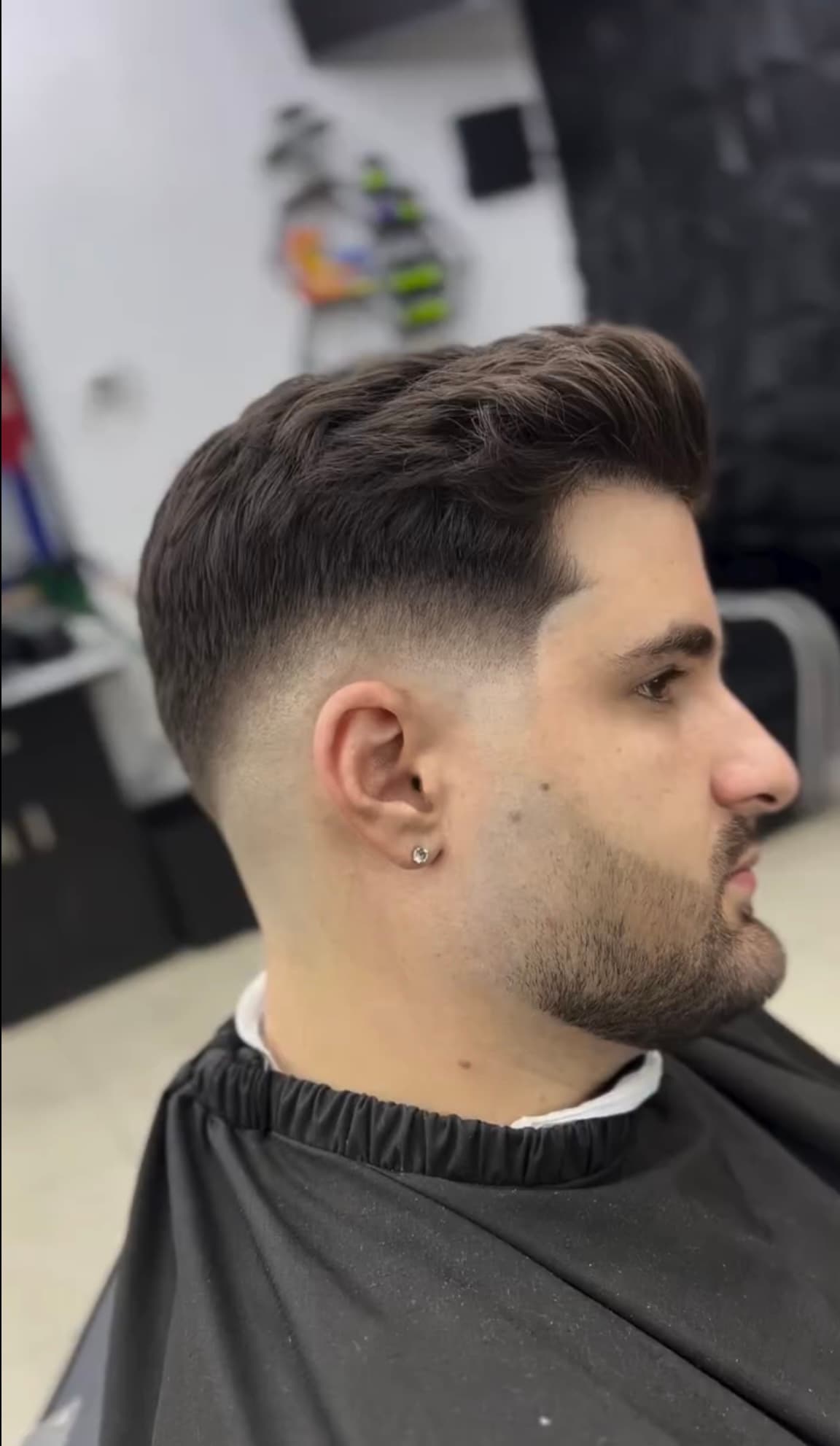 Mid skin fade con barba contorneada en capa de barbería